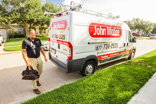 A John Moore Services technician walking from the service van to the house to fix a water heater with his tools.