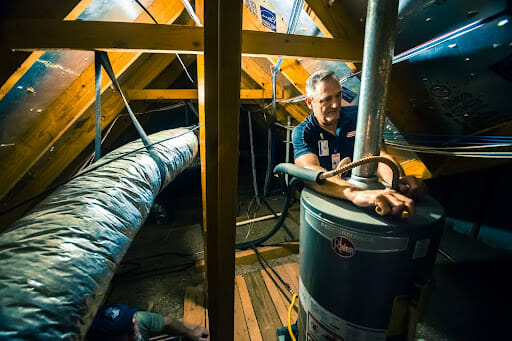 A John Moore Services technician working on a water heater fix the hot water in the house.